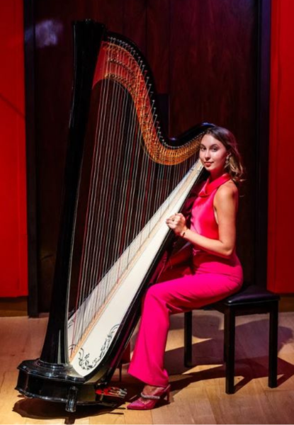 Amie true in pink suit sitting with harp